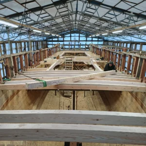 Kuva veneen rungon rakentamisesta pressun alla, joka näyttää yksityiskohtaisia puutöitä ja rakenteen edistymistä.